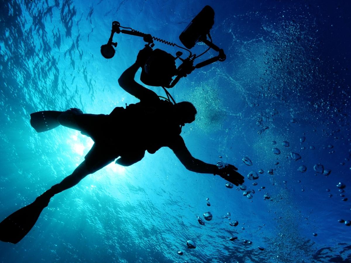 a diver with a camera underwater, surrounded by blue light, bidadari
