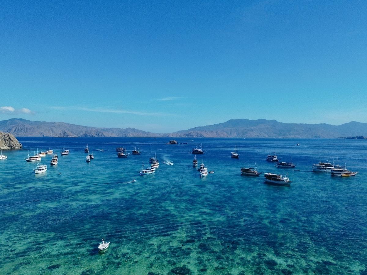 labuan bajo boats floating on clear blue water with distant mountains